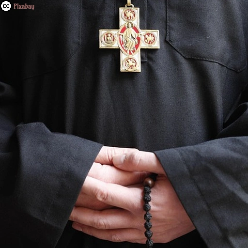 Eine Person, gekleidet in einer Mönchsrobe, mit einem christlichen Kreuz als Kettenanhänger vor der Brust und Rosenkranzkette in der Hand.