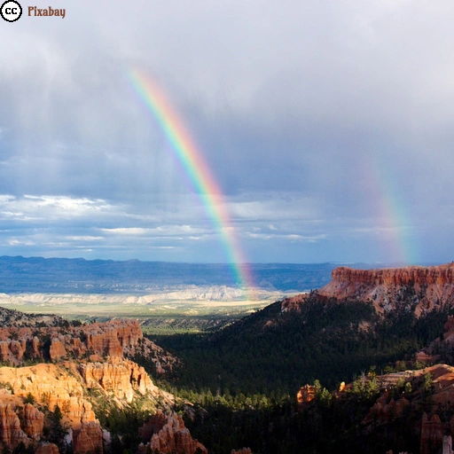 Der Bryce Canyon in Utah unter einem teils stark bewölkten Himmel. Ein doppelter Regenbogen erscheint über der Ebene hinter den roten Felsformationen.