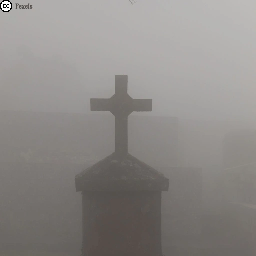 Ein Grabstein mit steinernem Kreuz steht in dichtem Nebel auf einem Friedhof.