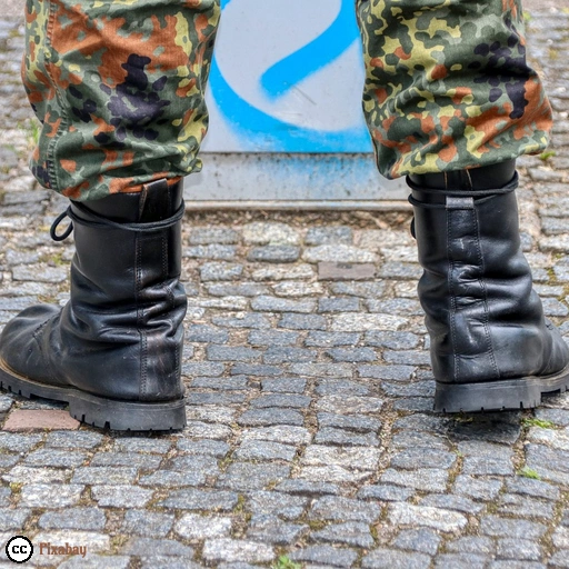Das Foto zeigt die Beine einer Person in der Uniform der Bundeswehr mit schwarzen Armeestiefeln auf einem gepflasterten Platz.